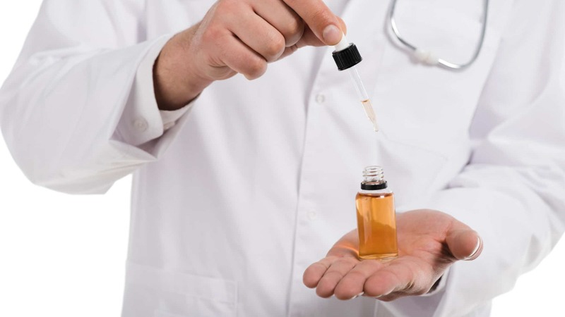 Doctor Holding CBD Oil on His Palm while Pulling the Pipette