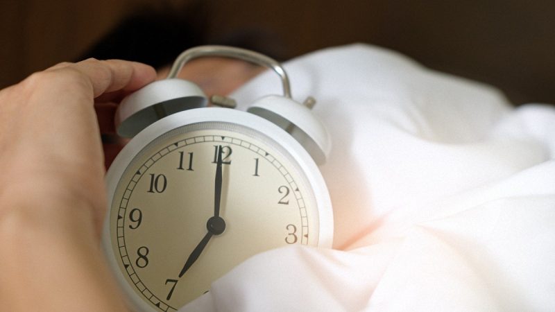 person holding an alarm clock in bed at seven in the morning