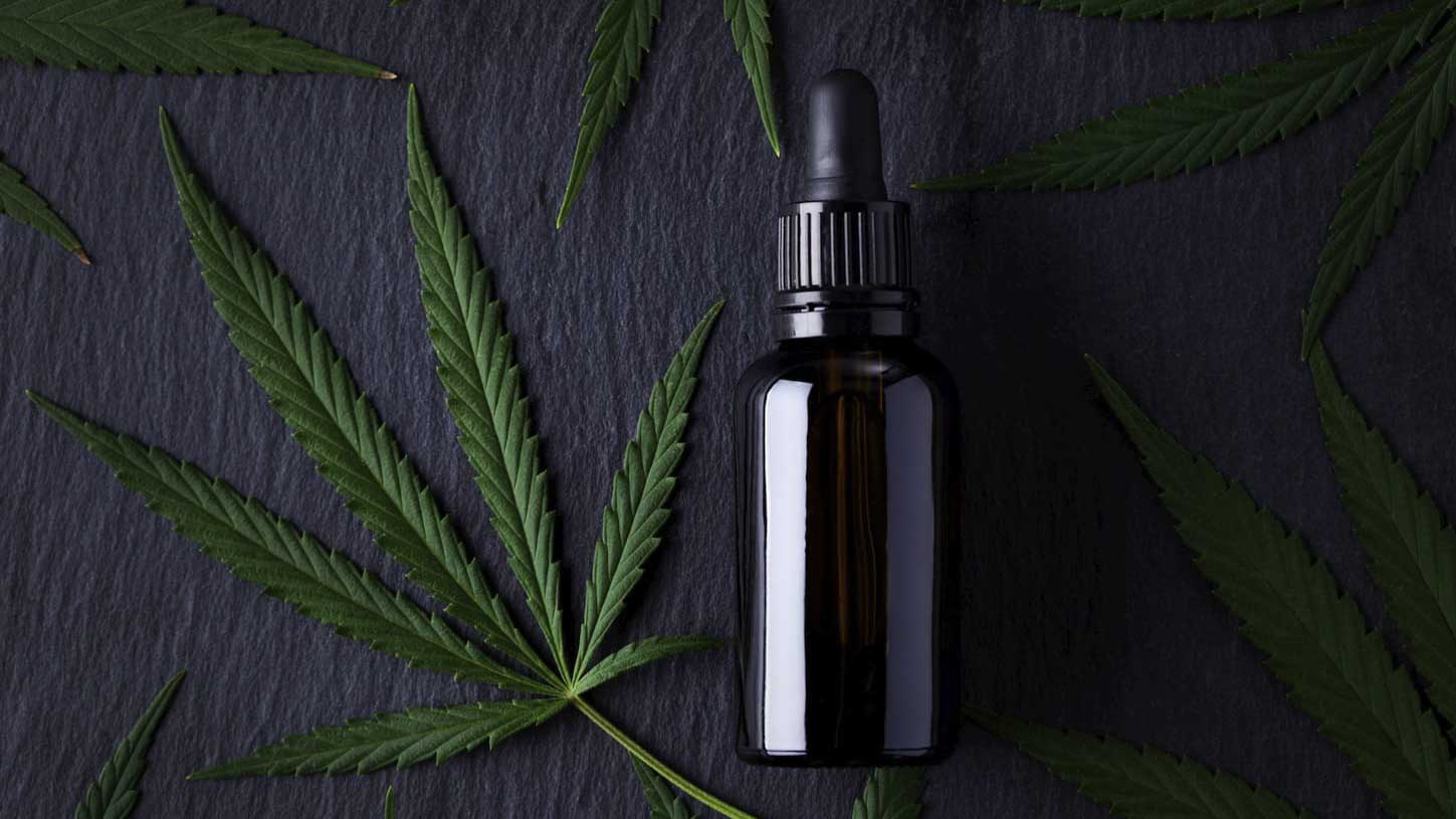 cbd oil next to a hemp leaf in grey background