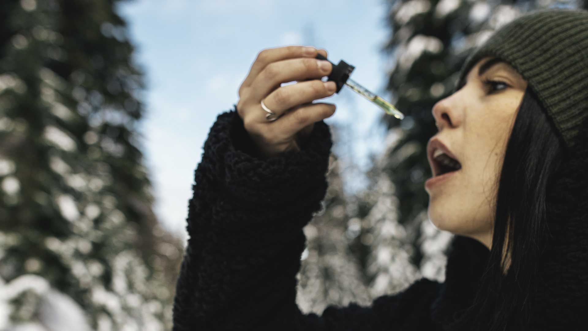 woman taking cbd from a dropper in a snow background