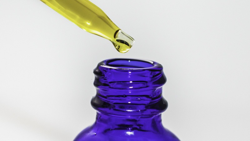 CBD oil from hemp dropping from a glass dropper into a blue glass bottle