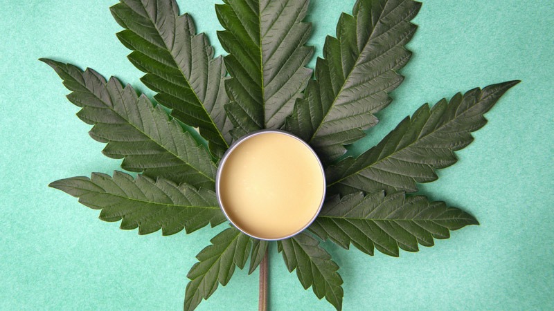 CBD Topical put in the center of a large hemp leaf in blue green background