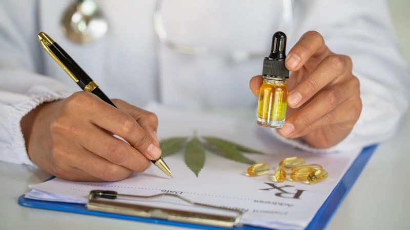 Doctor Writing on a Prescription Pad Holding CBD Oil