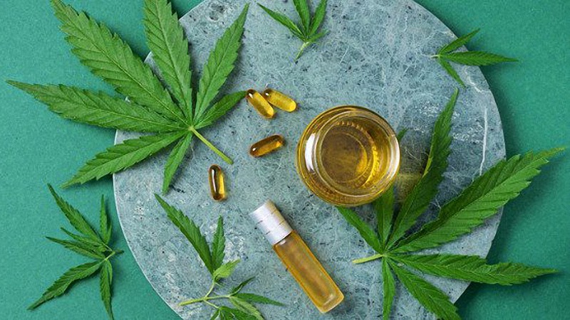 CBD Oil and Capsules with Hemp Leaves in Green Background