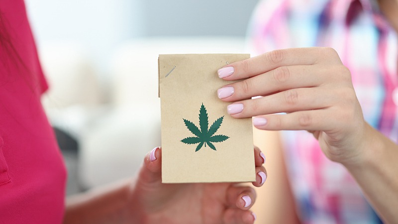 female hand holding paper bag with hemp print handed to another female