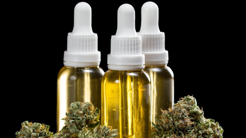 Three Bottles of CBD Oil with Hemp in a Black Background