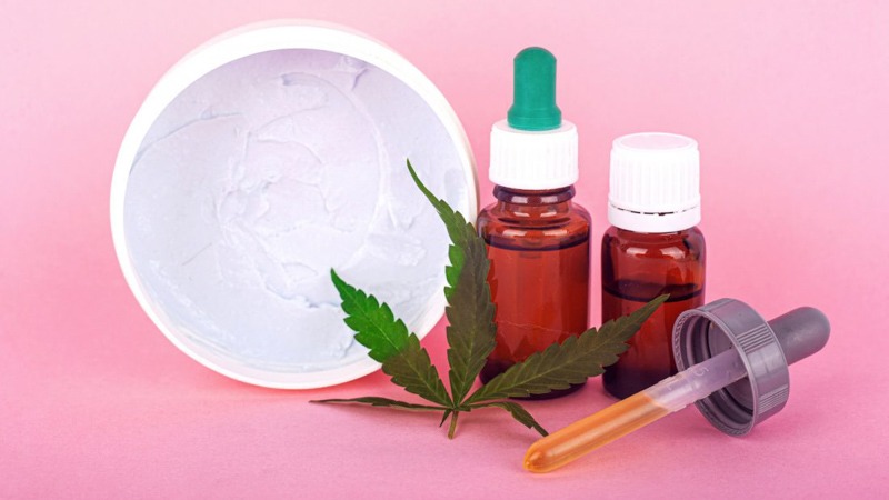 CBD oil and CBD cream with hemp leaf in pink background