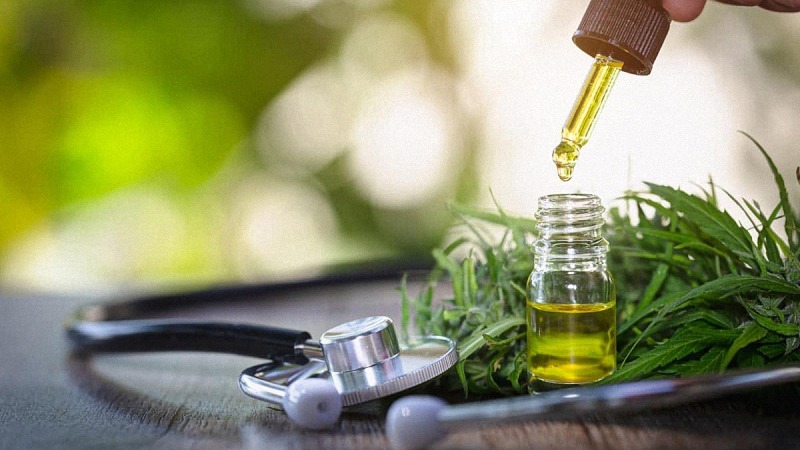 CBD oil dropper, cannabis leaves and a stethoscope on a wooden table