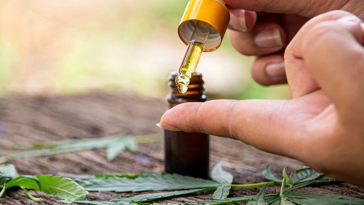 pouring a drop of CBD extract unto finger and a bottle with hemp leaves on the table